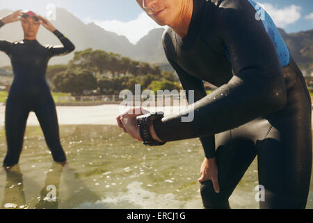 L'uomo controllando il suo timer. Gli atleti in mute la preparazione per il triathlon. Foto Stock