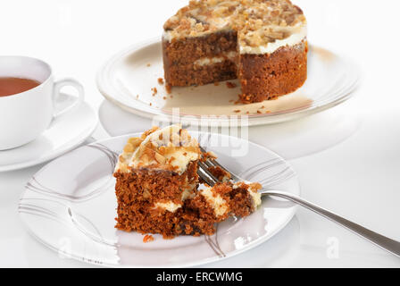 Torta di carote di fetta servita su una piastra con la forcella su una superficie bianca. Tazza di tè. Messa a fuoco selettiva Foto Stock