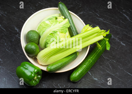 Un assortimento di verdure fresche a foglia verde in un vaso di ceramica su una pietra nera superficie Foto Stock