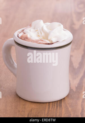 Cioccolata calda con panna topping in un antico cup su tavola in legno rustico Foto Stock