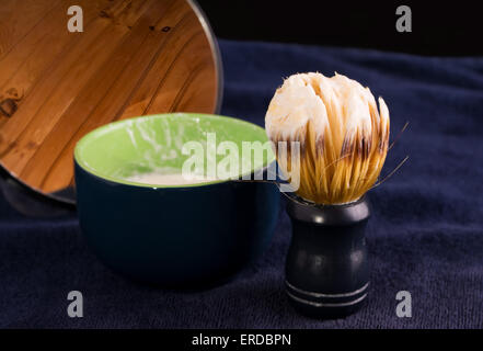 Spazzola per la rasatura con schiuma di sapone, bicchiere e specchio sul blu scuro asciugamano Foto Stock