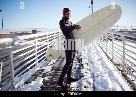 Nero ragazza adolescente in neoprene che trasportano le tavole da surf in inverno Foto Stock