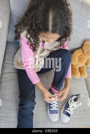 Razza mista ragazza legando le sue scarpe sul divano Foto Stock