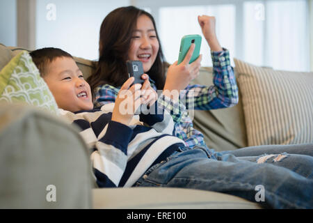 Asian fratello e sorella utilizzando i telefoni cellulari sul divano Foto Stock