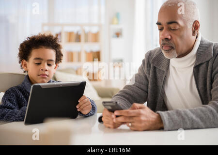 Razza mista nonno e nipote tramite telefono cellulare e la tavoletta digitale Foto Stock