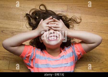 Sorridente ragazza ispanica che copre la sua gli occhi sul pavimento Foto Stock
