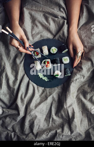 La donna a mangiare il sushi con bacchette in letto Foto Stock