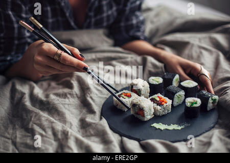 La donna a mangiare il sushi con bacchette in letto Foto Stock