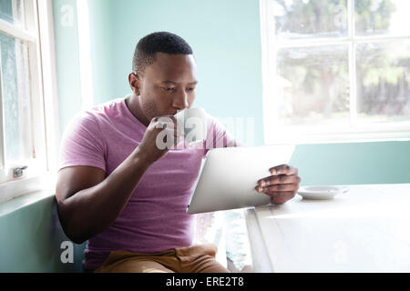 Uomo nero a bere caffè e con tavoletta digitale Foto Stock