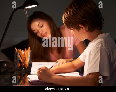 Sorella adolescente aiutare il fratello minore con studi presso la scrivania in camera da letto in serata Foto Stock