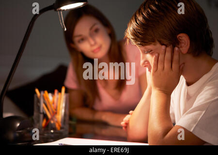 Sorella adolescente aiutando sottolineato fratello più giovane con studi presso la scrivania in camera da letto in serata Foto Stock