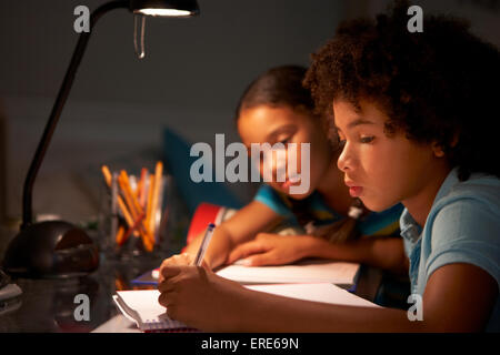 Due figli che studiano a scrivania in camera da letto in serata Foto Stock