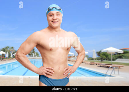 Giovane con una cuffia per la piscina e gli occhiali in posa di fronte a una piscina e sorridente Foto Stock