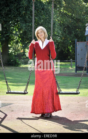 Una donna in rosso seduto su un altalena in un parco. Foto Stock