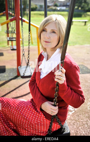 Una donna in rosso seduto su un altalena in un parco. Foto Stock