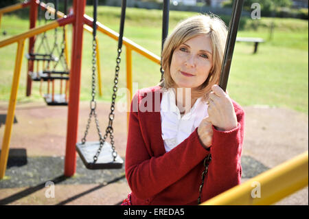 Una donna in rosso seduto su un altalena in un parco. Foto Stock