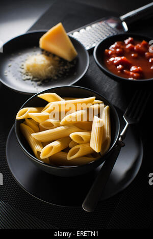 Penne la pasta con il sugo di pomodoro e formaggio parmigiano su sfondo nero Foto Stock