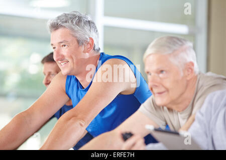 Tre felice personale senior di equitazione biciclette di filatura in palestra Foto Stock