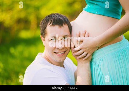 Ritratto di padre con guancia vicino a donne in stato di gravidanza la pancia di mia moglie. Incinta giovane. Felice la gravidanza. L uomo e la donna. Moglie e marito Foto Stock