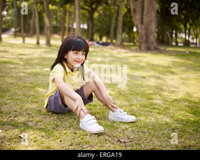 Poco ragazza asiatica si siede su erba nel parco. Foto Stock