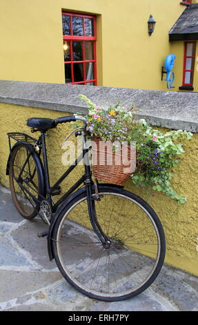 Vecchia bicicletta rustico con grazioso cesto fiorito appoggiata sulla parete gialla dell'edificio. Foto Stock