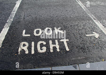 Asfalto con parcheggio gli spazi contrassegnati con la freccia e parole che leggere "guardare a destra' alle persone che attraversano street. Foto Stock