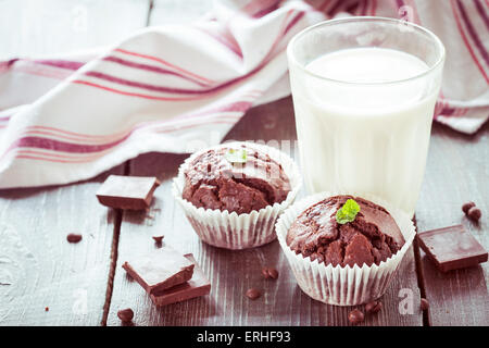 Un bicchiere di latte e due muffin al cioccolato su un tavolo di legno Foto Stock