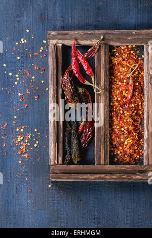 Assortimento di tutto asciutte e scaglie red hot chili peppers in una scatola di legno su blu scuro tela come sfondo Foto Stock
