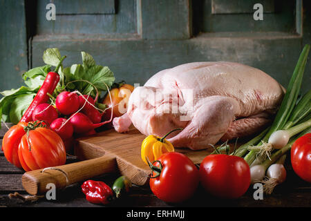 Materie giovane anatra sul tagliere di legno con fresche e mature le verdure sopra un tavolo di legno. Dark atmosfera rustica. Foto Stock