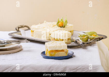 In casa fette di torta con mousse cremosa e frutti tropicali di mango e physalis servita nel vintage vassoio di metallo su tavolo bianco Foto Stock