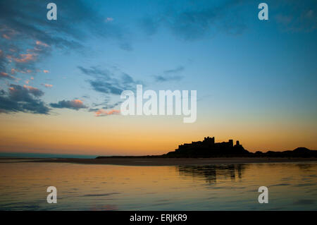 Il castello di Bamburgh stagliano afterglo del tramonto e riflessa nella sabbia bagnata della spiaggia con la bassa marea. Bamburgh, né Foto Stock