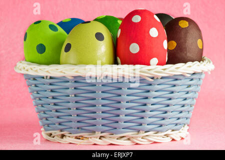 Le uova di pasqua su un bianco e blu cesto su sfondo rosa Foto Stock