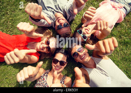 Sorridente amici mostra Thumbs up sdraiati sull'erba Foto Stock