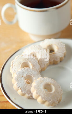 Italian canestrelli su un piattino vicino a una tazza di tè nero. Questi cookie hanno una forma di fiore e sono ricoperti di polvere Foto Stock