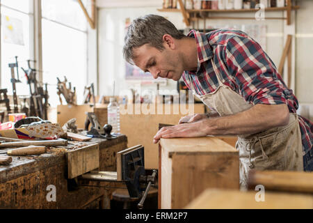 Un arredamento antico restauratore nella sua officina servendosi di un attrezzo a mano per smussare un oggetto di legno. Foto Stock