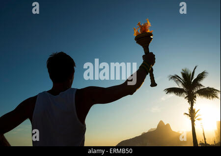 Silhouette di un atleta in piedi con la torcia di sport a Rio de Janeiro in Brasile skyline tramonto a Ipanema Beach Foto Stock