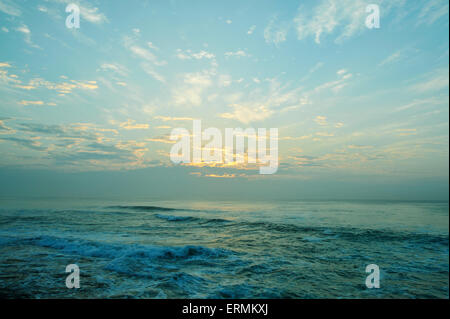 Bagliore dorato di mattina presto sunrise contro le nubi sull orizzonte, moody alba oltre oceano con le onde che si infrangono Foto Stock