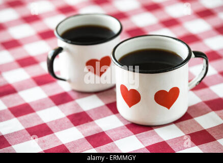 Caffè servito in smalto vecchio tazze con il cuore. Rosso e sfondo bianco. Foto Stock