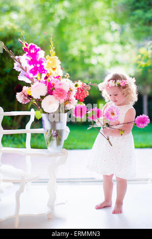 Bambina disponendo dei fiori a casa in un vaso. Bambini che giocano al chiuso. Kids festa di compleanno. I bambini dando fiore come presente. Foto Stock