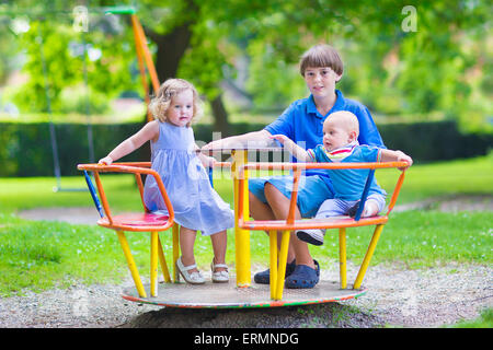 Tre bambini felici, fratelli e sorelle insieme giocando su un parco giochi swing gode di una posizione soleggiata caldo giorno d'estate Foto Stock