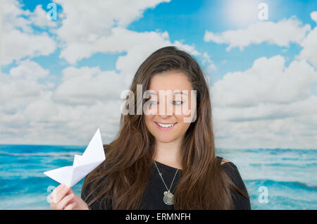 Bruna in possesso di una carta origami figura nella parte anteriore della Oceanic Sfondo nuvola Foto Stock