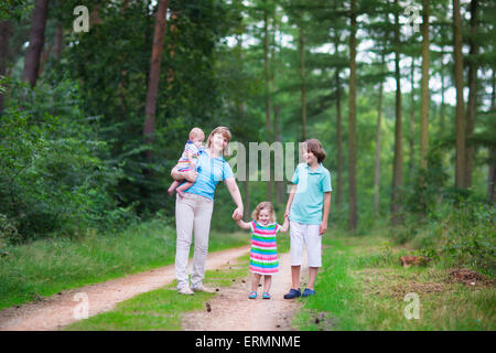 Felice donna attiva godendo di escursionismo con tre bambini in età scolare boy, toddler girl e piccolo bambino, passeggiate in legno di pino forest Foto Stock