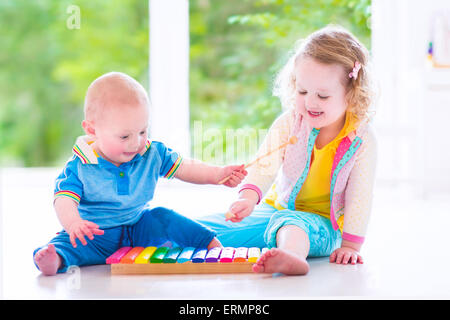 Due bambini piccoli - molto carino curly toddler girl e una divertente baby boy, fratello e sorella di riproduzione di musica con xilofono colorato Foto Stock