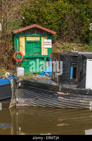 Un narrowboat ormeggiata lungo alcuni disordinato degli elementi da giardino Foto Stock