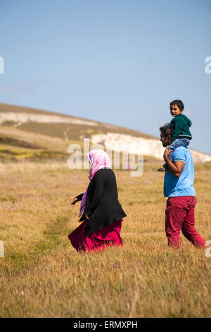 Uomo che trasporta un bambino sulle spalle con una donna che cammina attraverso i campi sulle scogliere della Freshwater Bay Cliffs a Isle of Wight, Hampshire, Regno Unito, a maggio Foto Stock