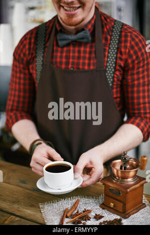 Sorridente barista azienda tazza di caffè nero con il macinino da caffè nelle vicinanze Foto Stock