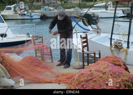 Pescatore cretese rammendo reti sulla banchina con la sua barca come sfondo a Georgioupoli Creta Grecia Foto Stock