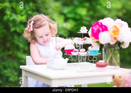 Adorabili bimbi divertenti ragazza con i capelli ricci che indossa un abito colorato per il suo compleanno giocando tea party con un orsacchiotto di peluche bambola Foto Stock