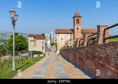 Muro di mattoni lungo la passerella di ciottoli e chiesa parrocchiale su sfondo sotto il cielo blu in Piemonte, Italia settentrionale. Foto Stock