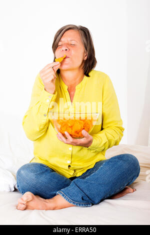 Donna seduta nel letto mangiare patatine Foto Stock